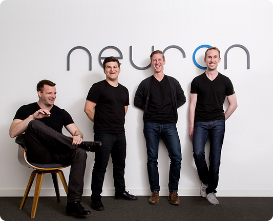 Photo of Neuron UX partners in an office with the Neuron logo on a white wall behind them